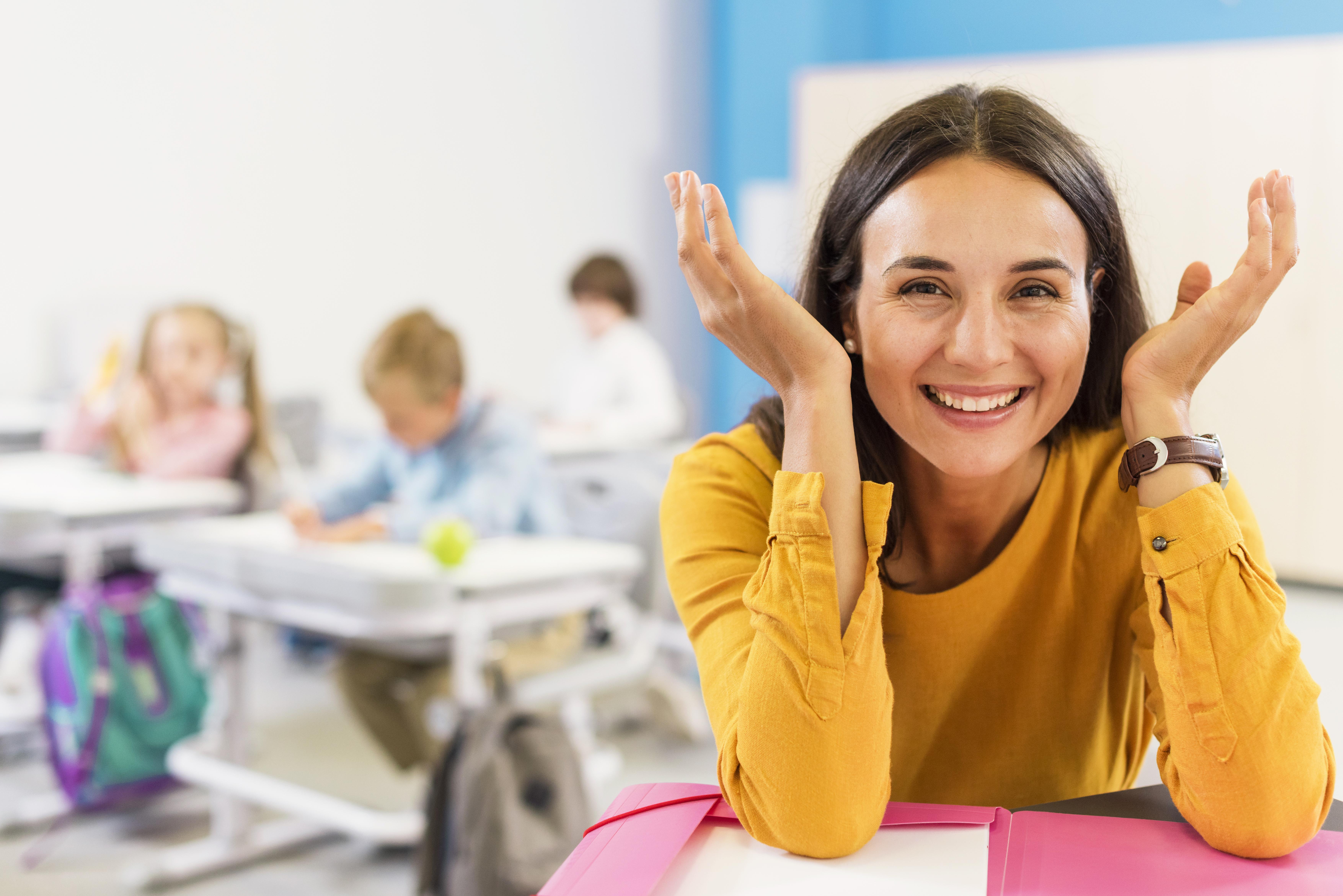 Glückliche Lehrerin sitzt an ihrem Schreibtisch.